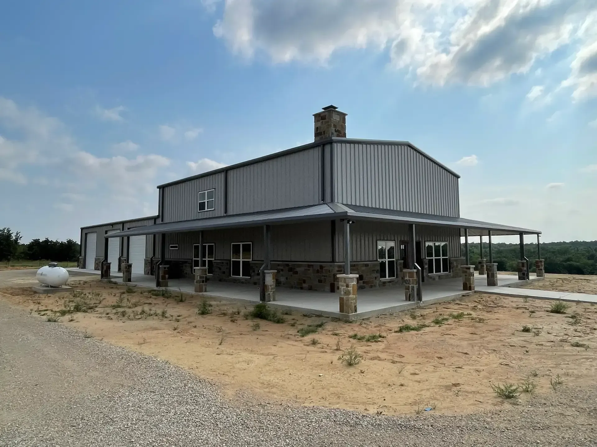tall two story tan and brown barndominium with a chiminy and large wrap around porch